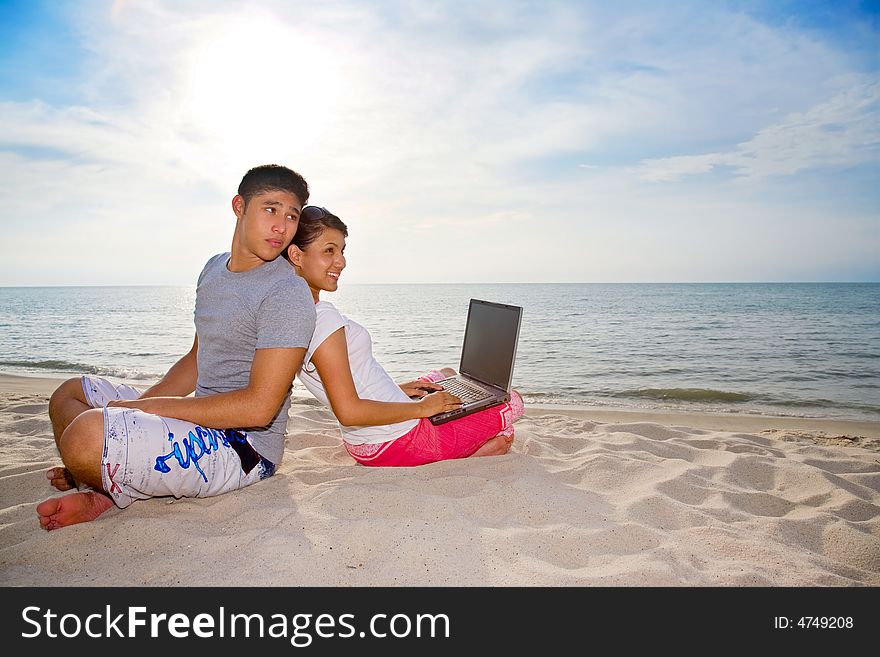 Couple relaxing on the beach while one of them haapily working on laptop. Couple relaxing on the beach while one of them haapily working on laptop