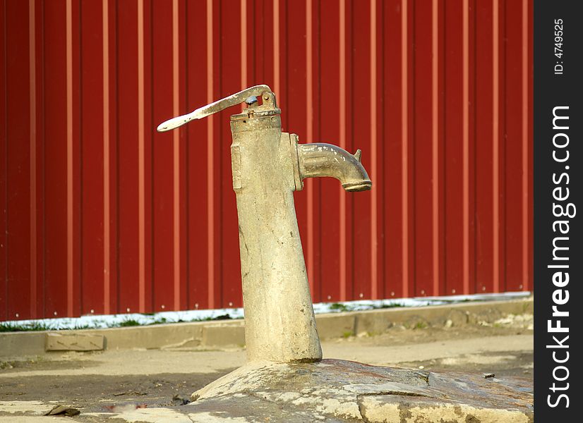The old water pump on a background of a red wall