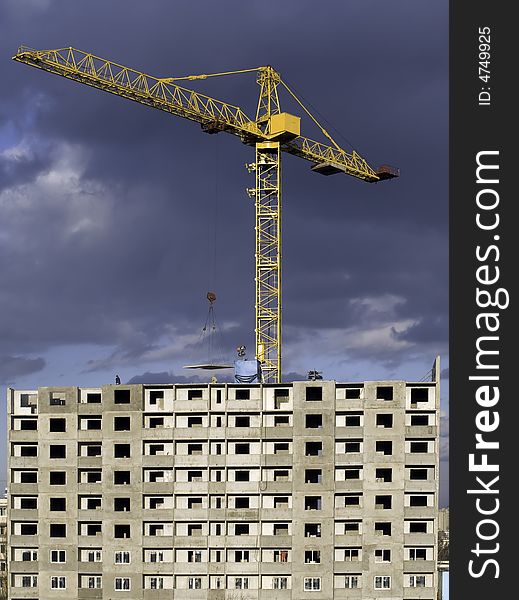 Hoisting crane lifting a concrete slab on a house being built, on the background of gloomy thunder clouds. Hoisting crane lifting a concrete slab on a house being built, on the background of gloomy thunder clouds