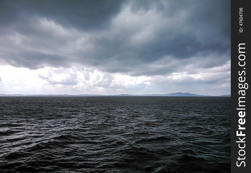 An angry looking black sea with threatening storm clouds overhead and distant hill on the horizon.