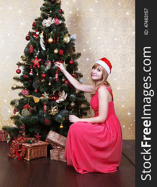 Young beautiful girl in Santa hat and pink dress sitting near Christmas tree. Young beautiful girl in Santa hat and pink dress sitting near Christmas tree