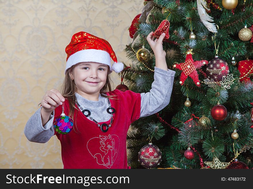 Little girl in Santa hat and red dress near Christmas tree. Little girl in Santa hat and red dress near Christmas tree