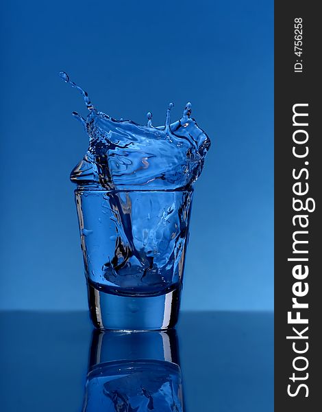 Glass with splashing water over  blue