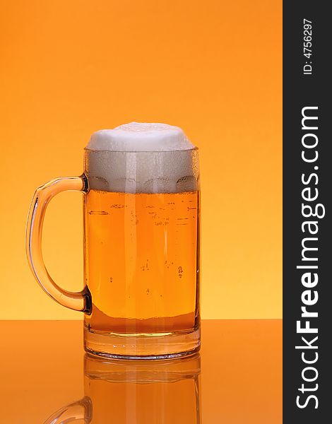 Mug of beer with froth over orange background