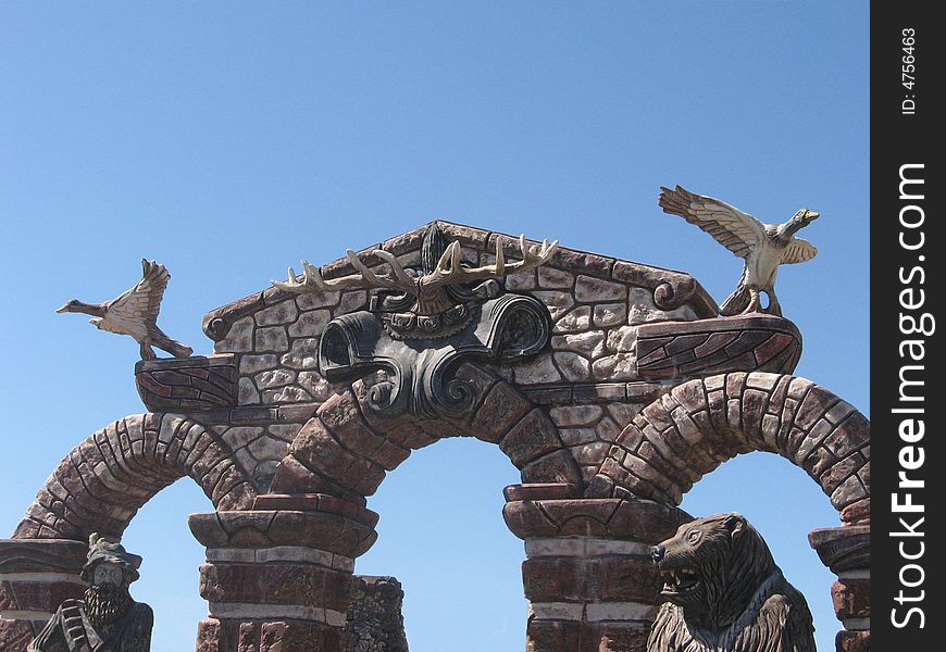 Beautiful stone gate. From above two wooden statues of ducks are installed. From below a statue of the hunter and a statue of a bear