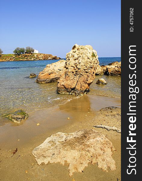 Big stones on the shore of Agios Apostolis beach with the chapel as background