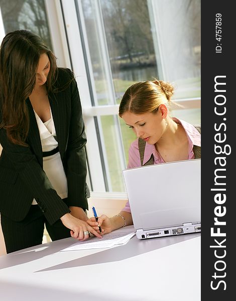 A successful business woman and her secretary with a document on a table with a laptop