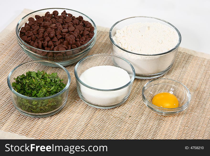 Various ingredients in glass bowls. Including flour, mint leaves, chocolate chips, egg and sugar. Various ingredients in glass bowls. Including flour, mint leaves, chocolate chips, egg and sugar.