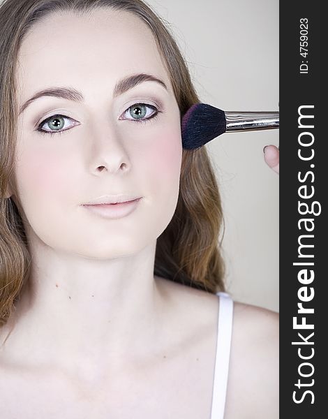 Young woman with green eyes and long brown hair getting her make-up done by a make-up artist � blush application. Young woman with green eyes and long brown hair getting her make-up done by a make-up artist � blush application