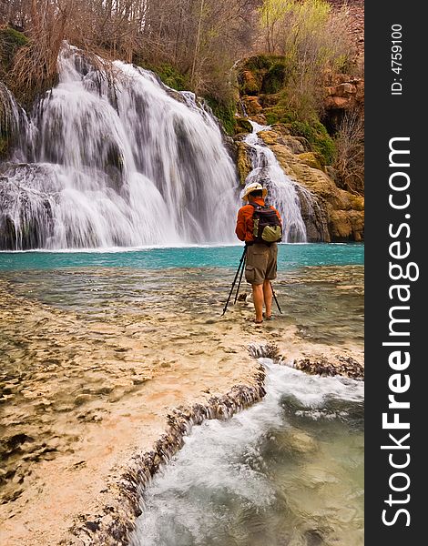 Young man standing in the water and photographing a beautiful waterfall. Navajo Falls - Havasu Canyon, Arizona. Havasupai Reservation. Young man standing in the water and photographing a beautiful waterfall. Navajo Falls - Havasu Canyon, Arizona. Havasupai Reservation.