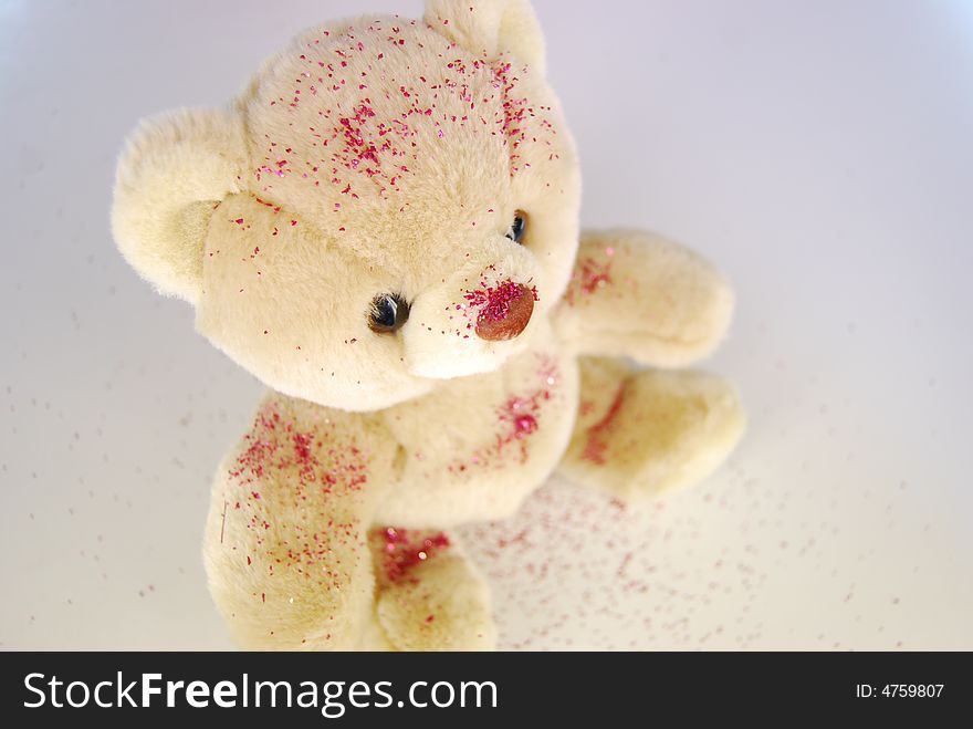 A soft beige teddy-bear with red glitter poured over on a white background. A soft beige teddy-bear with red glitter poured over on a white background