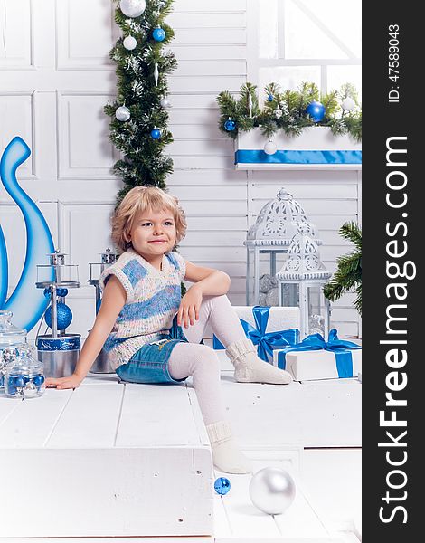 Little smiling girl sitting next to a Christmas tree and Christmas toys. Little smiling girl sitting next to a Christmas tree and Christmas toys