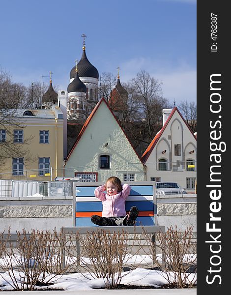 Early mild spring at  the center of Old Town little girl become sunburnt on chaise longue in the middle of snow