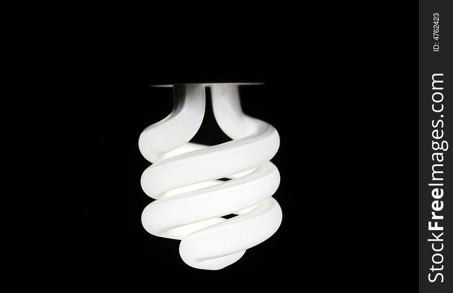 Glowing compact fluorescent bulb hanging upside down against a dark background