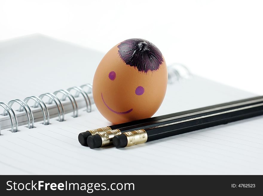 Smiley egg with black pencils on note book. Smiley egg with black pencils on note book