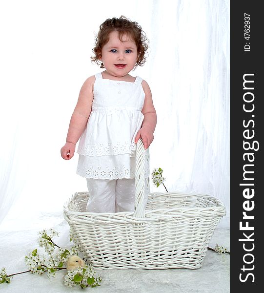 Baby girl in wicker basket in front of white background with flowers on floor and chick perched on flowers. Baby girl in wicker basket in front of white background with flowers on floor and chick perched on flowers