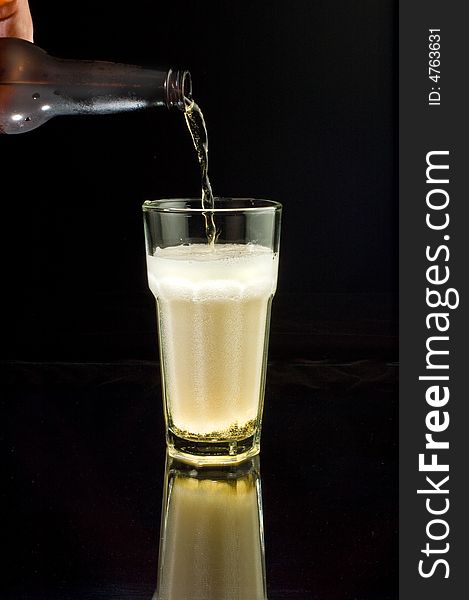 Pouring an ice-cold beer into a glass, isolated against black with reflection. Pouring an ice-cold beer into a glass, isolated against black with reflection