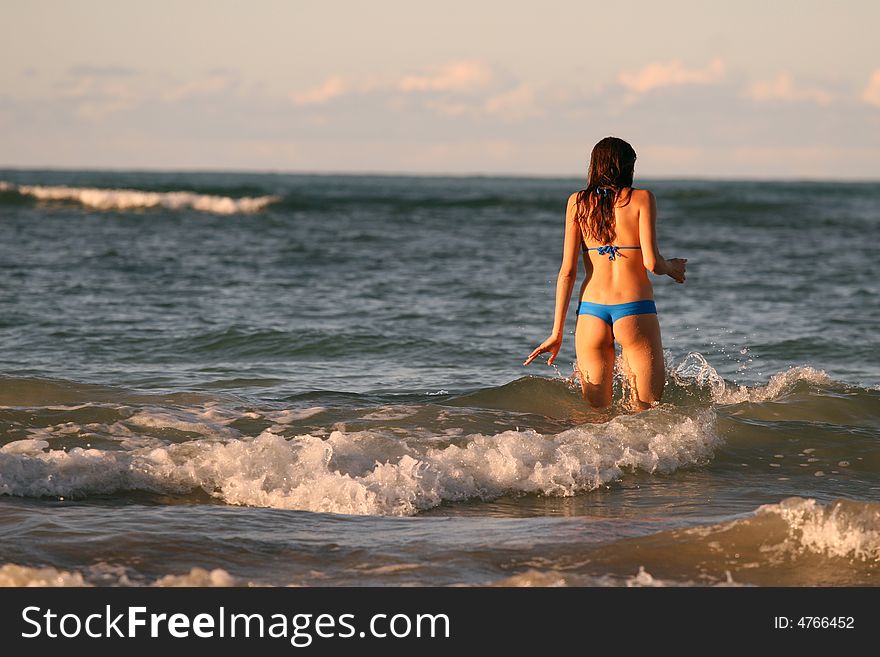 Young woman goes in ocean to swim by sunset. Young woman goes in ocean to swim by sunset