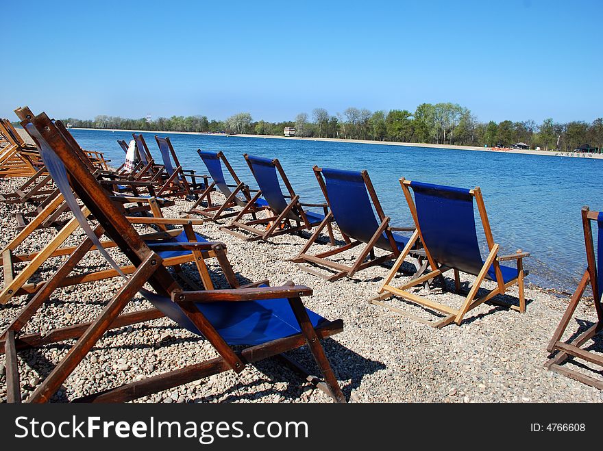 Blue folder chairs row on stone beach by lake. Blue folder chairs row on stone beach by lake
