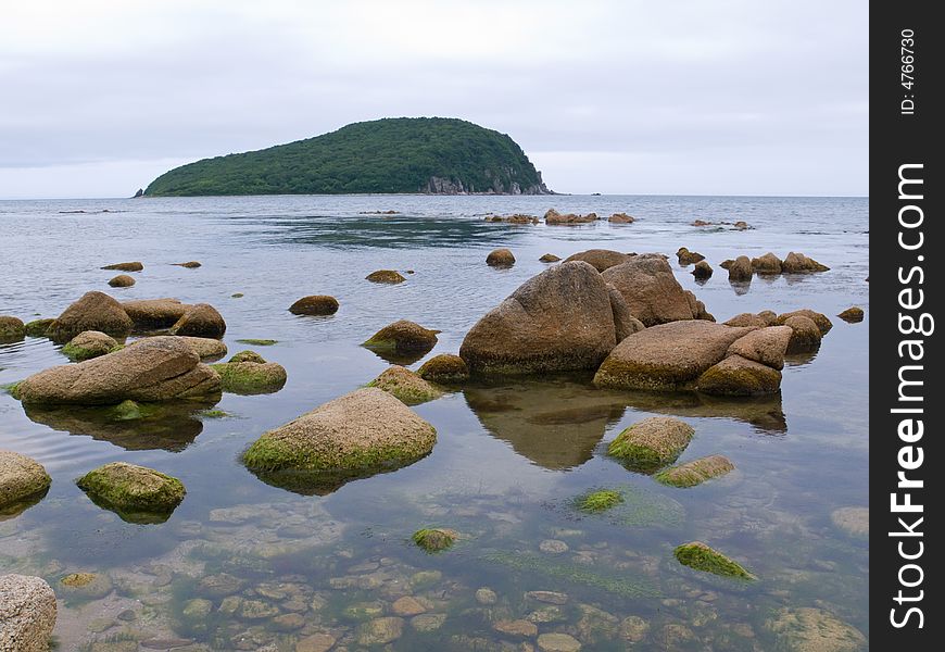 A close-up of the stones in sea. On background is green island. Russian Far East, Primorye, nature state reserve Lazovsky, Petrova island. A close-up of the stones in sea. On background is green island. Russian Far East, Primorye, nature state reserve Lazovsky, Petrova island.