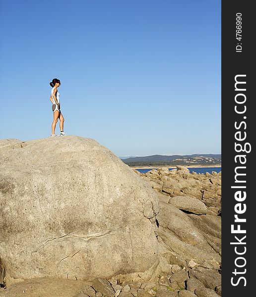 A woman stops to enjoy the view after climbing to the top of a rock. A woman stops to enjoy the view after climbing to the top of a rock