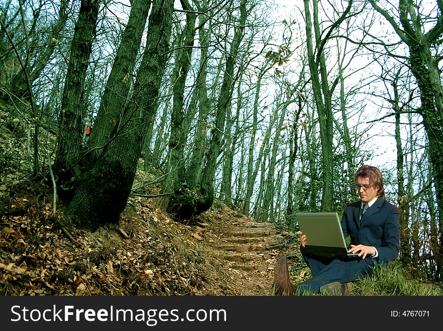 A business man with a laptop in a wood. A business man with a laptop in a wood