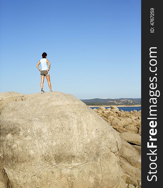 A woman stops to enjoy the view after climbing to the top of a rock. A woman stops to enjoy the view after climbing to the top of a rock