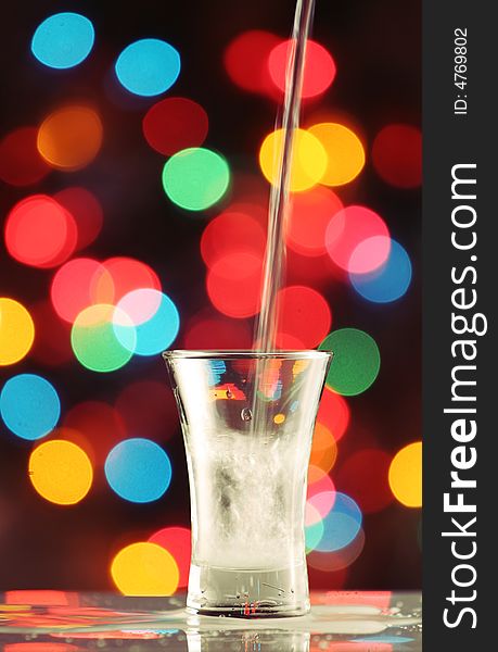 Pouring a seethrough liquid in to a shot glass, fairy light background, please check for more. Pouring a seethrough liquid in to a shot glass, fairy light background, please check for more