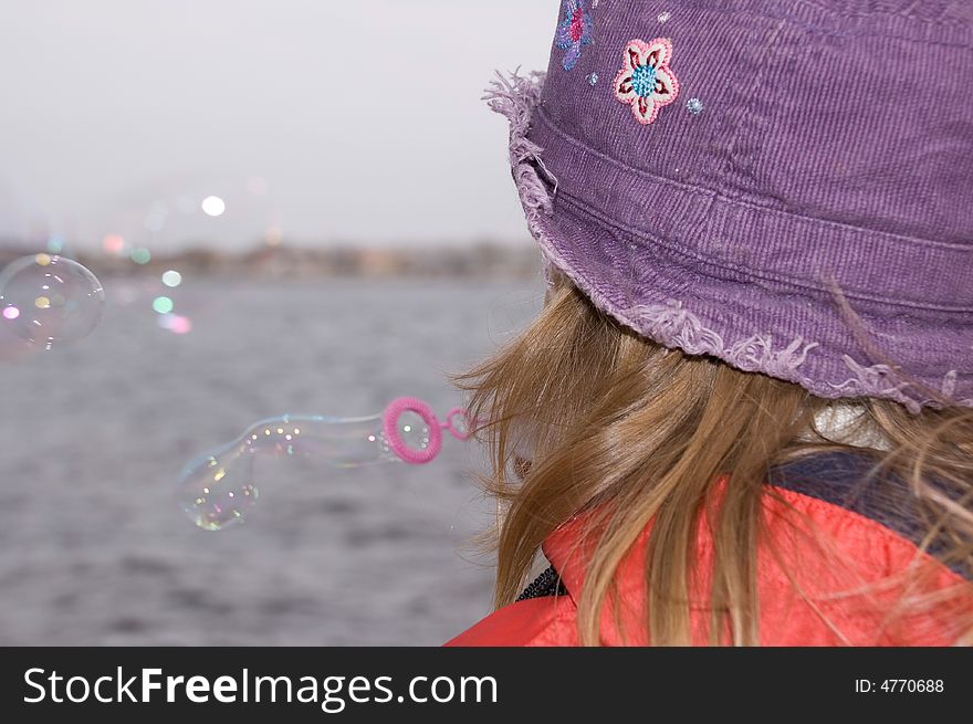 Child blowing soap bubbles out on the river bank