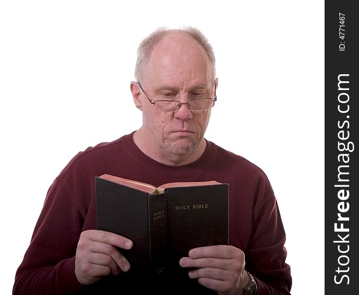 An older bald man in a red shirt and glasses reading the bible on a white background. An older bald man in a red shirt and glasses reading the bible on a white background