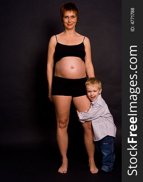 A pregnant woman with her child holding her leg. A pregnant woman with her child holding her leg