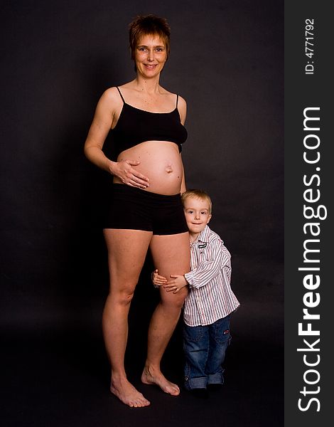 A pregnant woman with her child holding her leg. A pregnant woman with her child holding her leg