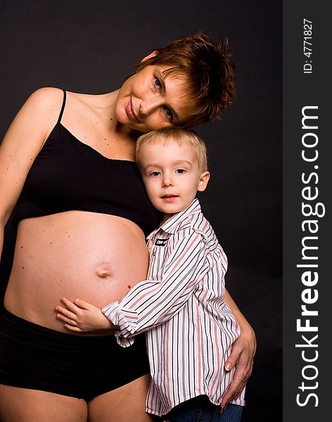 A pregnant woman holding her son next to her. A pregnant woman holding her son next to her.