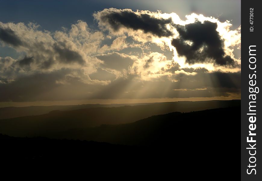 Sunbeams from behind clouds, with distant hills