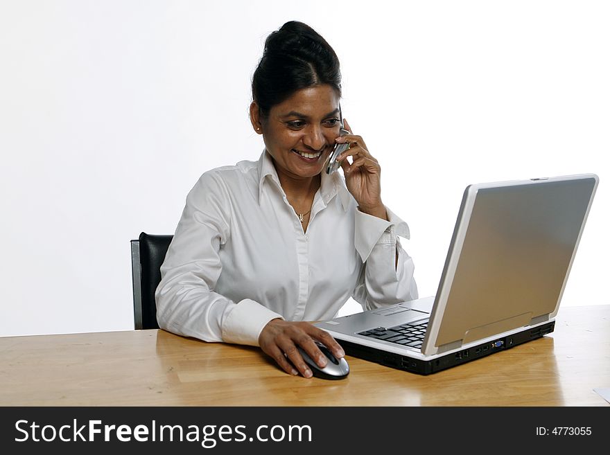 Indian woman chatting on the phone and smiling while working on her laptop. Indian woman chatting on the phone and smiling while working on her laptop