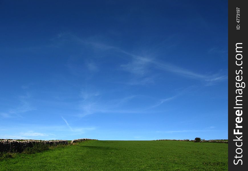 Saturated blue sky and green field with wall
