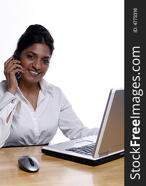 Indian business woman smiling on her cell phone while working at her laptop. Isolated against a white background. Indian business woman smiling on her cell phone while working at her laptop. Isolated against a white background