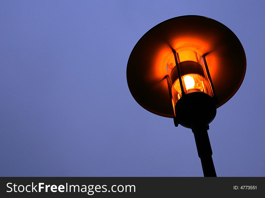 Street lamp isolated against pale blue sky with a soft orange glow.