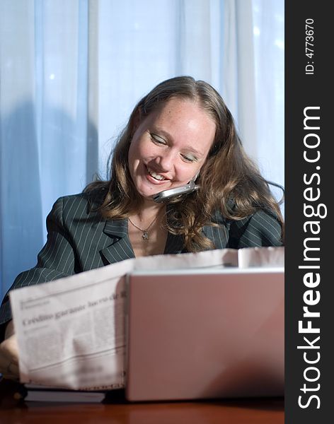 A woman, talking on a cellphone, sitting holding a newspaper behind a laptop. A woman, talking on a cellphone, sitting holding a newspaper behind a laptop.