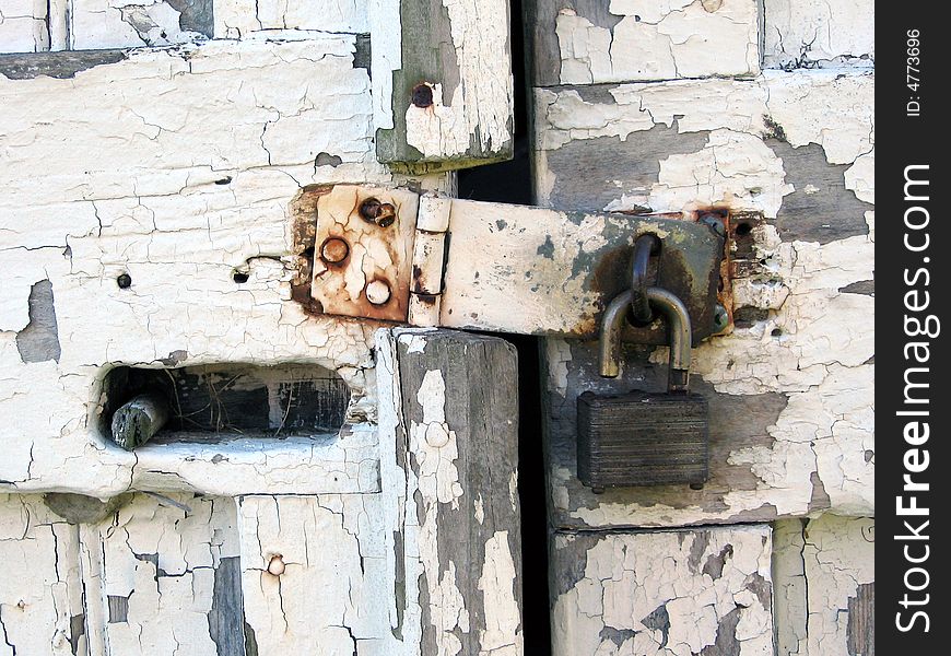 A shot of an isolated unlocked padlock, securing a shed, made of wood, with white peeling paint. A shot of an isolated unlocked padlock, securing a shed, made of wood, with white peeling paint.