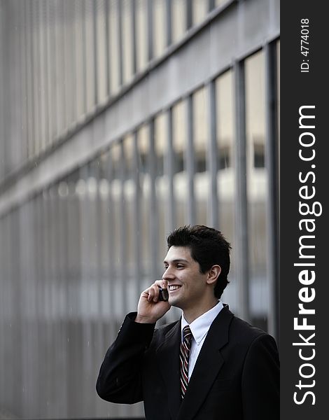 Male caucasian business man smiling while talking on his cell phone while standing outside an office building in the rain. Male caucasian business man smiling while talking on his cell phone while standing outside an office building in the rain