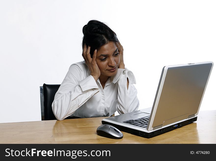East Indian business woman sitting in front of her laptop holding her head in her hands. Isolated against a white background. East Indian business woman sitting in front of her laptop holding her head in her hands. Isolated against a white background