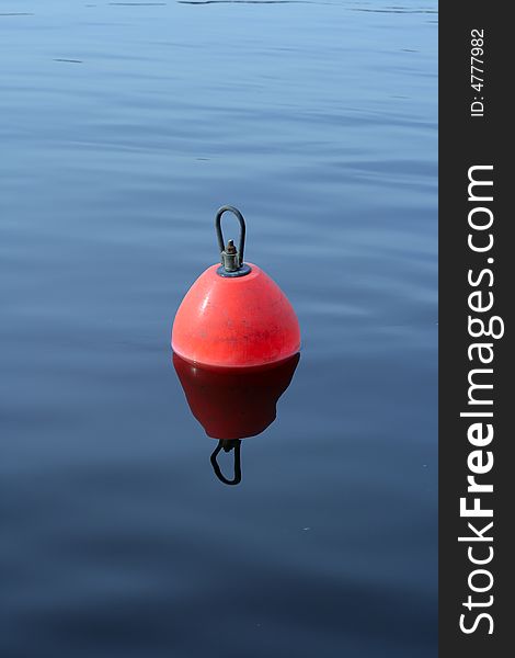 Red-orange plastic buoy with iron loop on the blue water. Red-orange plastic buoy with iron loop on the blue water
