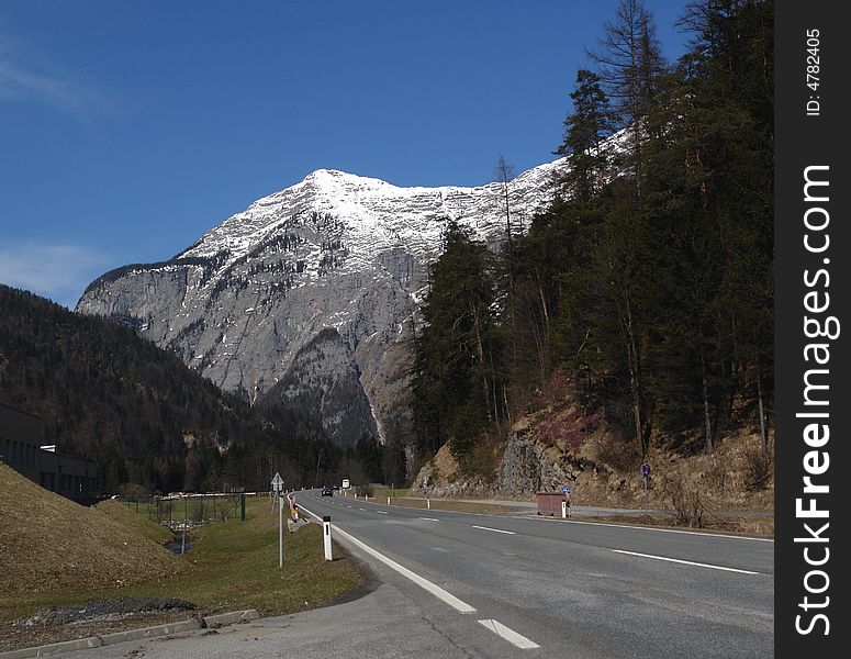 Road under the Peak of mountain at the background of blue sky . Alpes in Austria . The Snow on the Rocks. Road under the Peak of mountain at the background of blue sky . Alpes in Austria . The Snow on the Rocks.