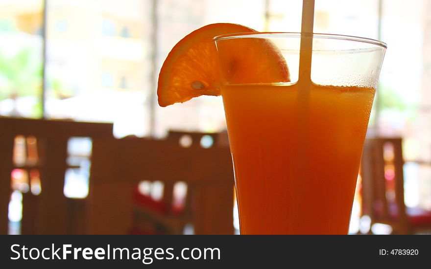 Orange juice in a clear glass with a straw in it, shot with a depth of field wooden background. Orange juice in a clear glass with a straw in it, shot with a depth of field wooden background.