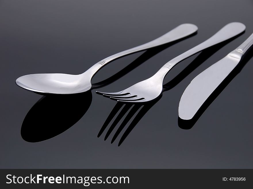 Modern silver spoon, knife, fork on the mirror background