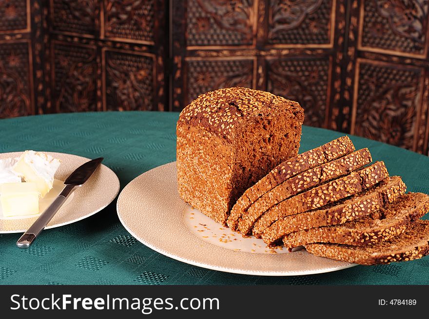 Freshly baked sliced wholegrain bread on a plate.  Sliced camerbert cheese and fresh butter in the background.