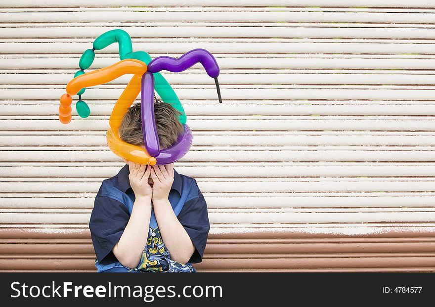 Young boy wearing a balloon hat hides his face. Young boy wearing a balloon hat hides his face