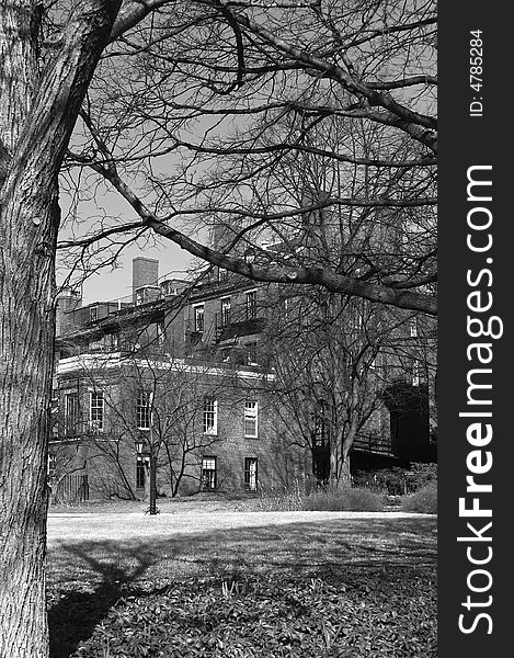 Haunting new england image of large old brick building hidden in the trees in black and white. Haunting new england image of large old brick building hidden in the trees in black and white
