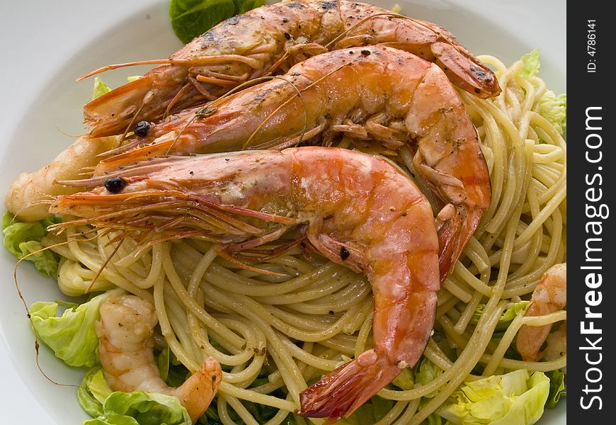 Cooked shrimps on spaghetti with salad on a white plate